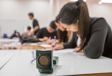 Student sitting at a table writing while a small piece of equipment is in the foreground