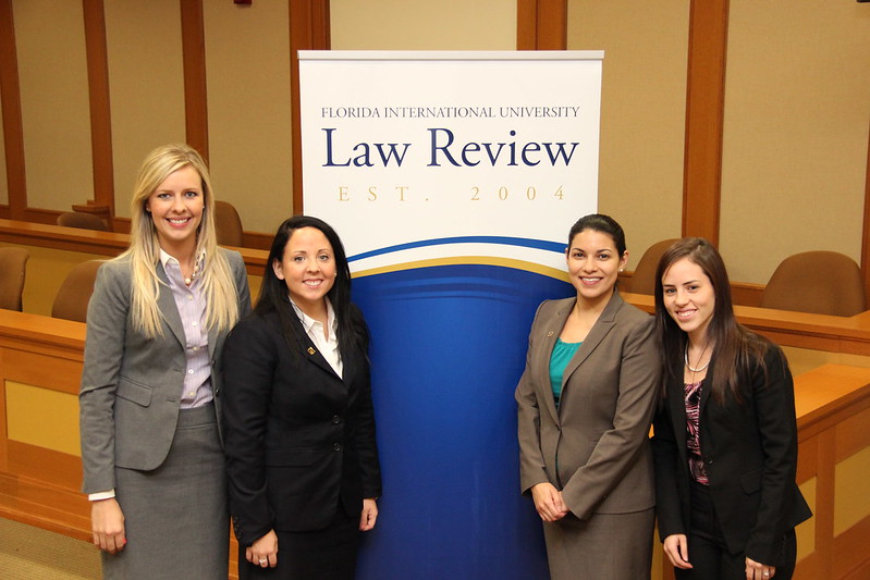 Group of women, three of them, standing in front of a banner that reads Florida International University College of Law, they are smiling and looking directly at the camera.