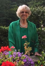 A smiling elder women wearing a bright green suit jacket