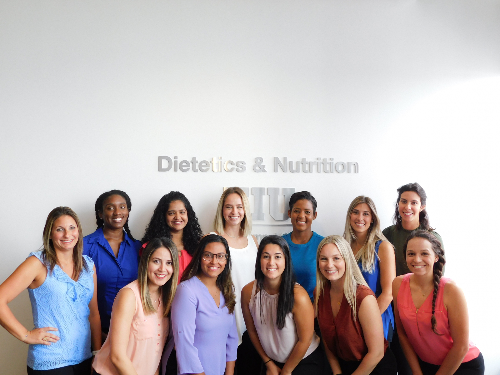 Group of female students standing in front of a sign on a white wall that says dietetics and nutrition 
