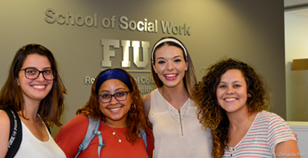 group of female students standing in close proximity in front of the social work school sign smiling brightly at the camera