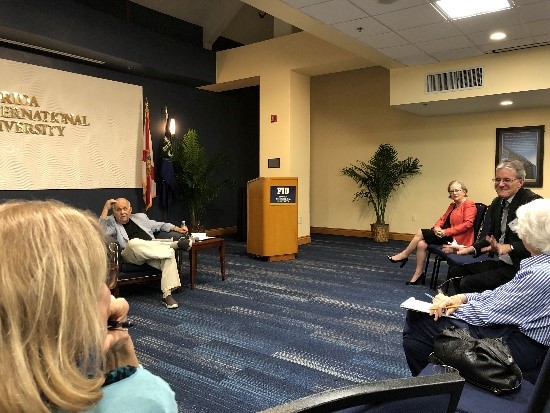 Group of faculty members sitting in a circle looking to the main speaker sitting i a lounge chair at the front of the room.
