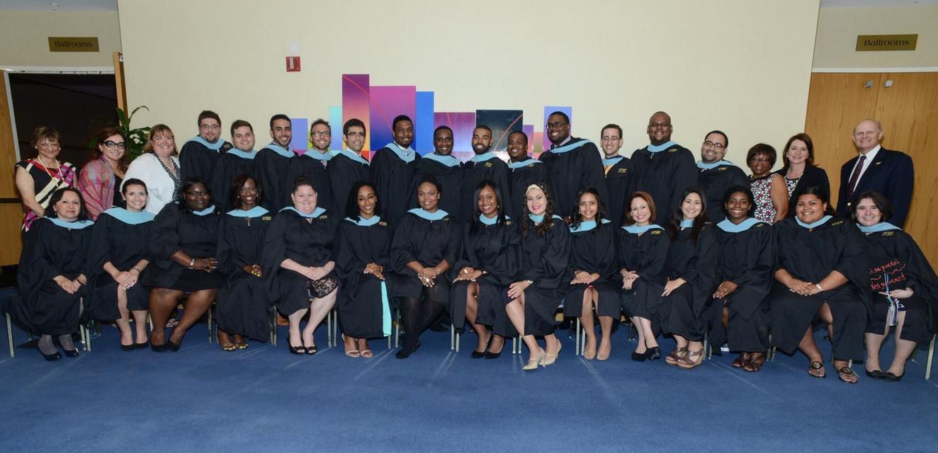 Dr. Lunsford standing outside the Graham Center Ballrooms with a class of recent graduates wearing their gowns.